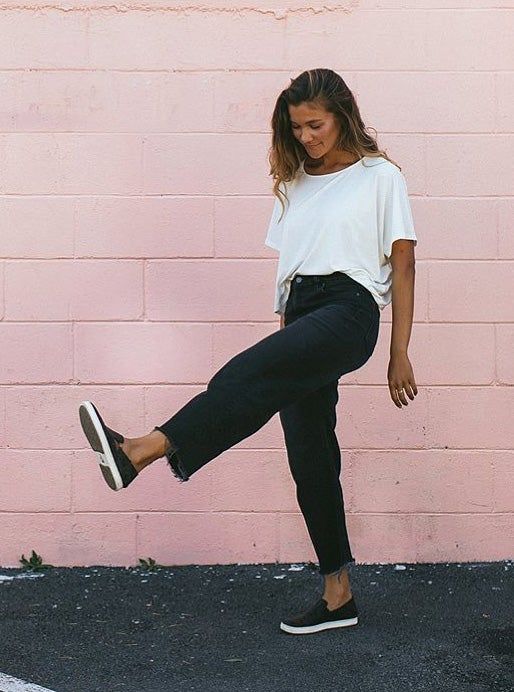 A model showcases the black sneakers against a vibrant pink wall, kicking their feet in a playful manner.