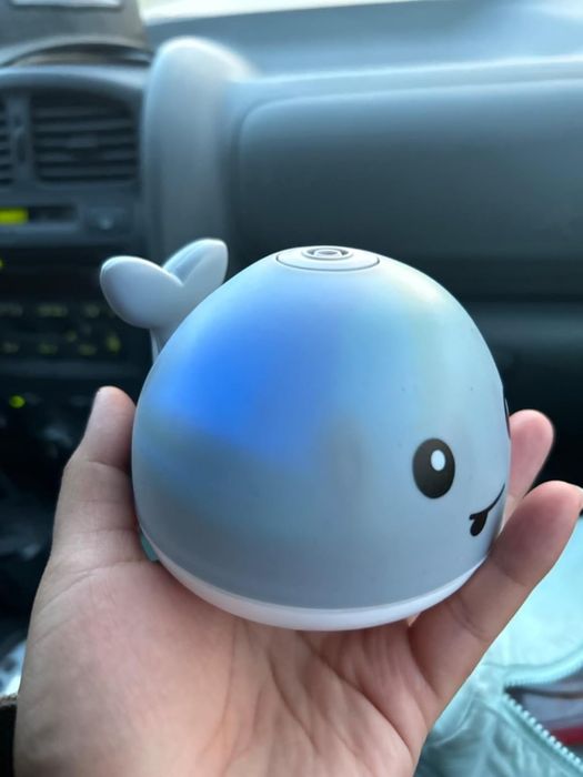 A hand holding a small, whale-shaped portable light with a smiley face, while in the car. Featured in a shopping article