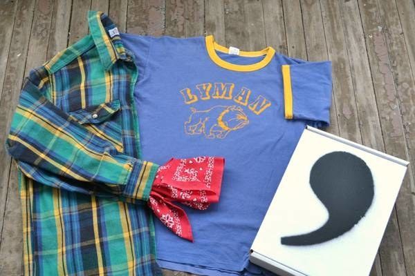 A flannel shirt, t-shirt, and bandana placed next to a box branded with the Comma logo.