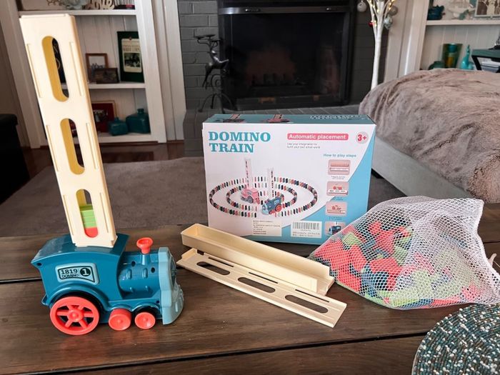 A domino train toy set displayed on a table with the box and domino pieces in a mesh bag, ready to be set up in a living room