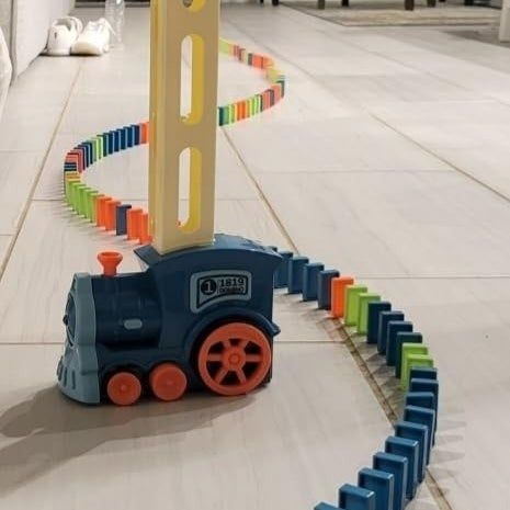 A toy train laying down colorful dominoes in a winding pattern on a tiled floor in a modern living room