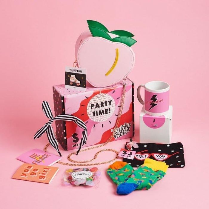 A pink box filled with socks, a mug, a peach-shaped purse, and a collection of other colorful goodies.