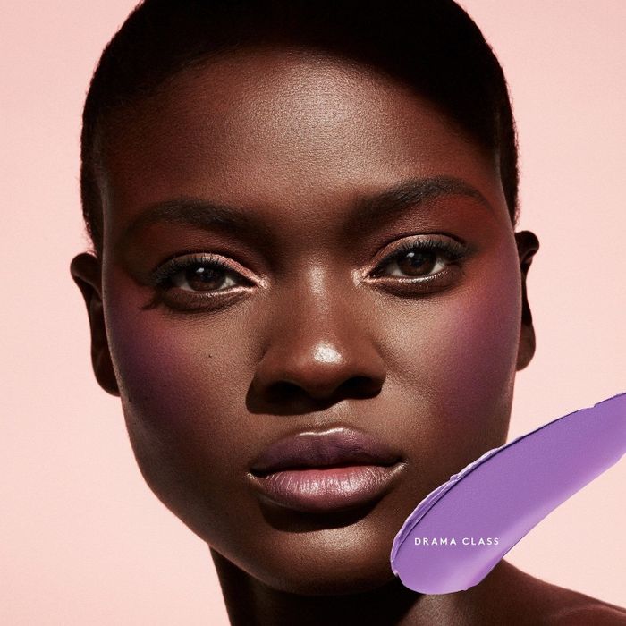 A model with deep brown skin wearing the purple shade of Cheeks Out Freestyle Cream Blush.