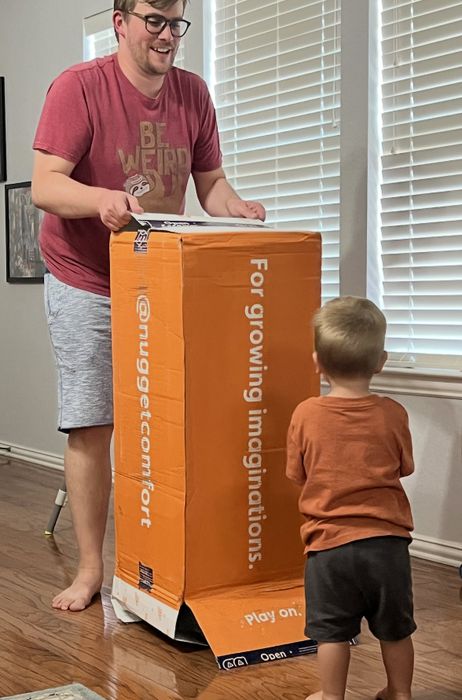 An adult and child playing with a large box labeled 