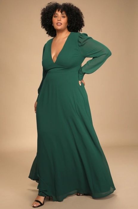 An image of a model wearing a long-sleeve maxi dress featuring sheer sleeves, a V-neckline, and an elegant low back