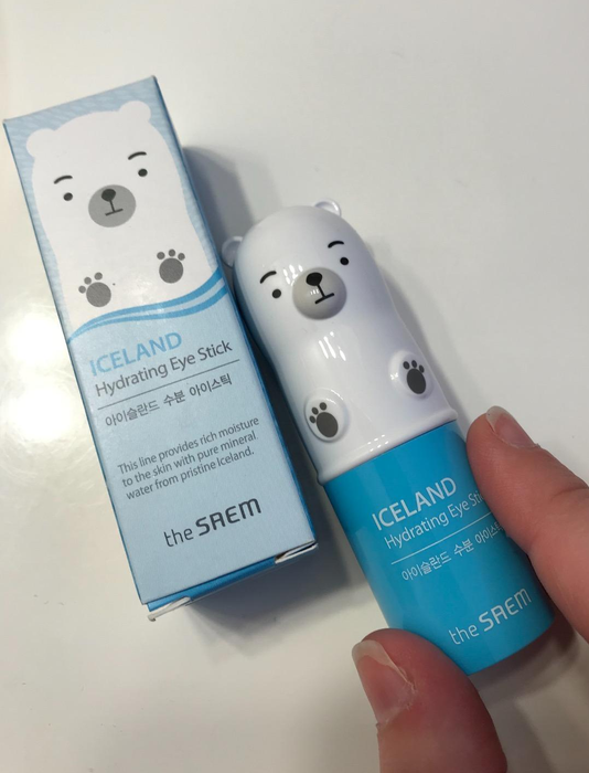 A person holding The SAEM Iceland Hydrating Eye Stick with a bear design next to its packaging.