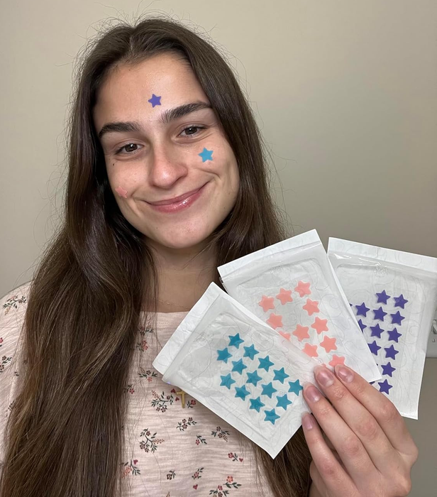 A reviewer holding the pack of pimple patches, sporting a couple of them on their skin