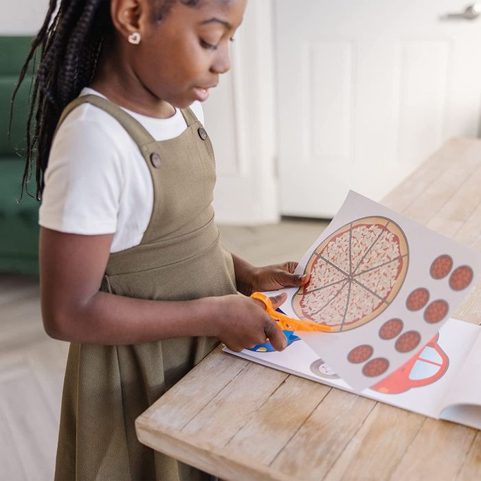 A child model practicing with safety scissors, cutting out pizza-shaped pieces.
