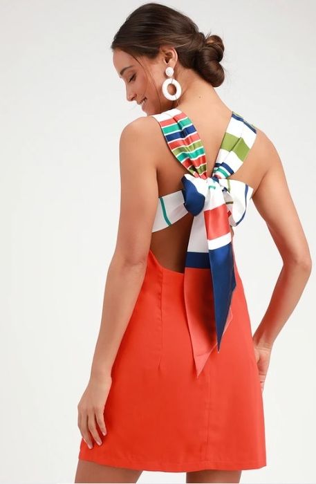 A model posing in a red-orange dress adorned with a stylish sash, exuding elegance and charm.