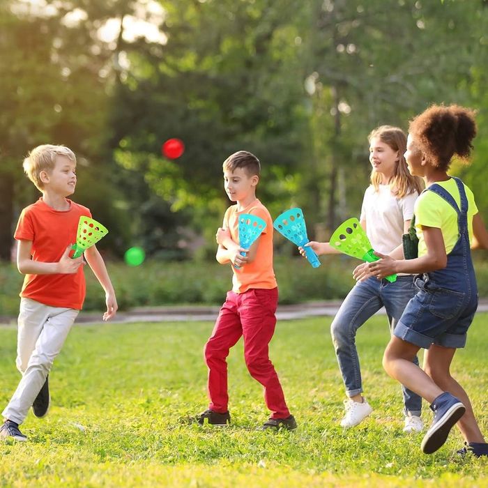 Four kids having fun outside, tossing green and red balls with their blue and green catchers.