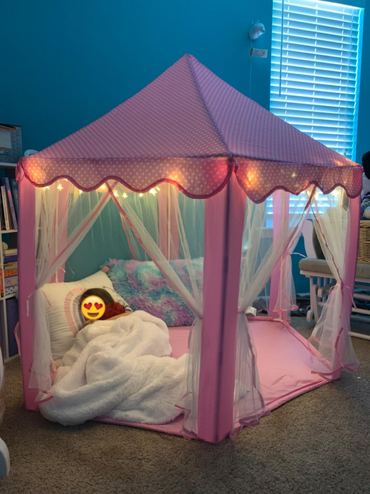 The reviewer’s child is cuddled up in the cozy pink tent, glowing softly from the lights around it.