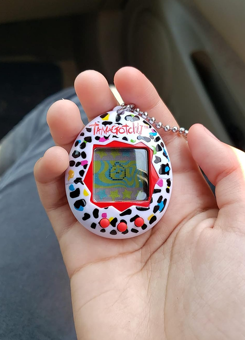 A reviewer showing off the Tamagotchi, holding it in their hand.