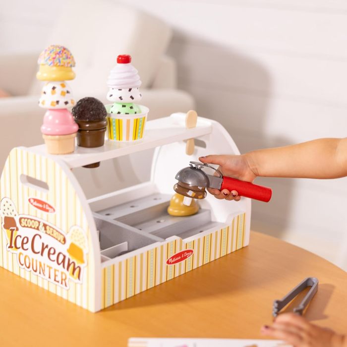 A child's hand using the ice cream scoop, playing with the counter set.