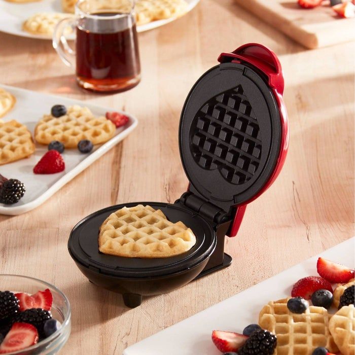A heart-shaped waffle maker surrounded by fresh berries.