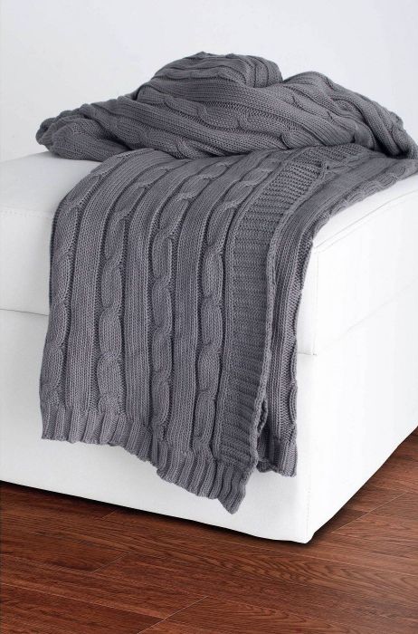 A soft gray cable-knit blanket laid out in a cozy home setting.
