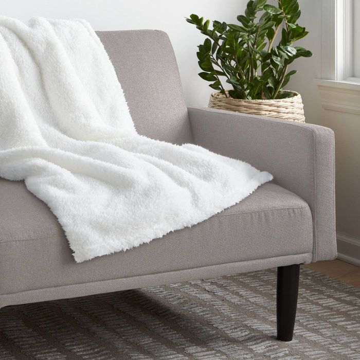 A soft, white blanket resting on a grey couch, ready for a cozy moment.