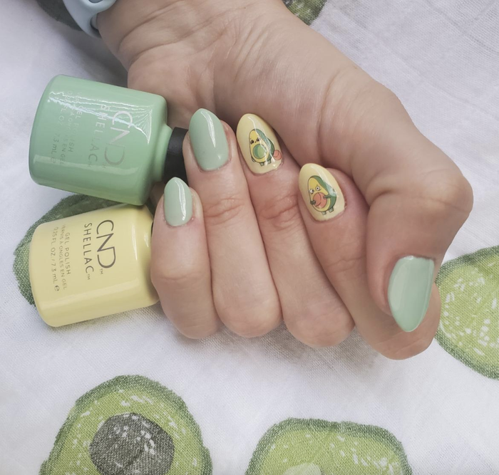 A reviewer's yellow and green manicure adorned with avocado stickers.