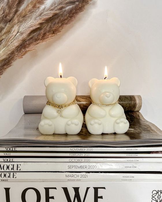 Two candles designed like bears sitting atop a stack of magazines.