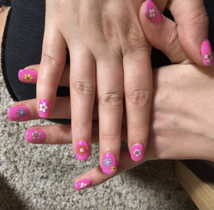 A reviewer's manicure featuring a pink color with flowers on each nail.
