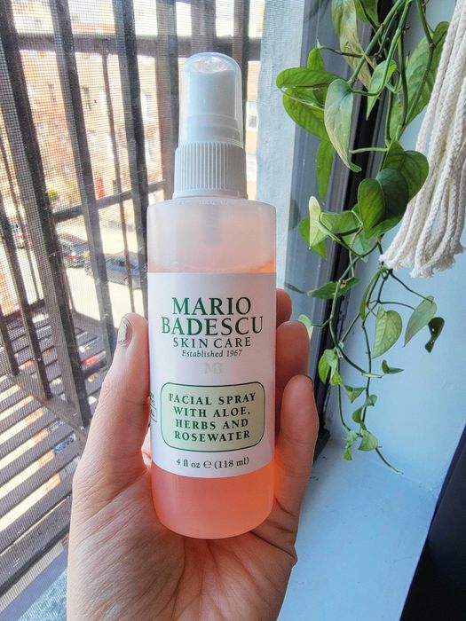 A hand holding a bottle of Mario Badescu facial spray.