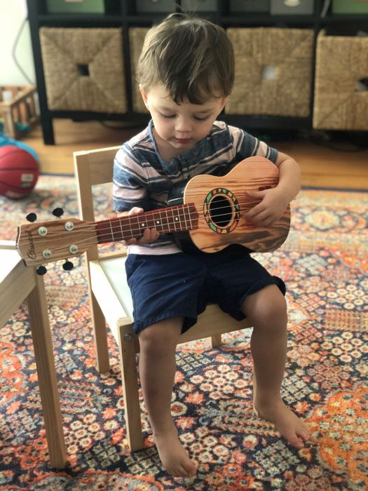 A young boy sits in a chair and plays a ukulele