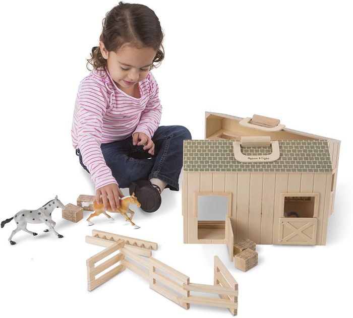 A child plays with a toy stable containing two toy horses