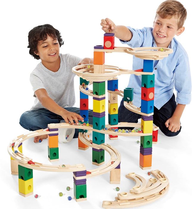 Two kids having fun while playing with marbles on a wooden marble run set.