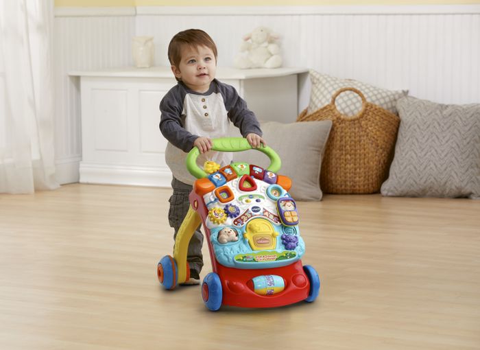 A toddler happily using an activity walker to move across the living room floor.