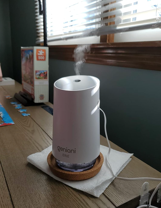 A white humidifier emitting steam on a table next to a puzzle box and scattered puzzle pieces.