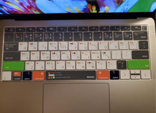 A silicone keyboard cover available in white, black, green, and orange, featuring tiny text displaying shortcut information directly on the keys.