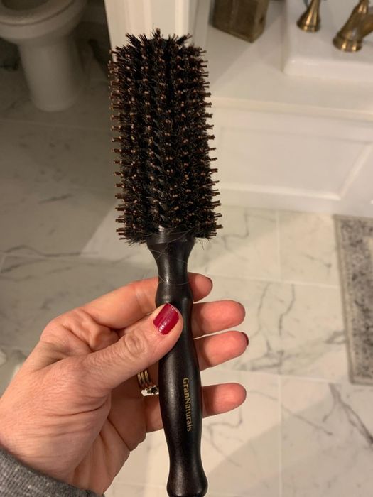 Person holding a bristle hairbrush with a sleek black handle