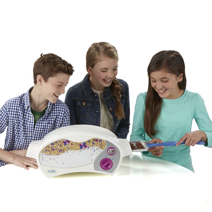 Three kids having fun with an Easy-Bake oven, placing a tray inside.