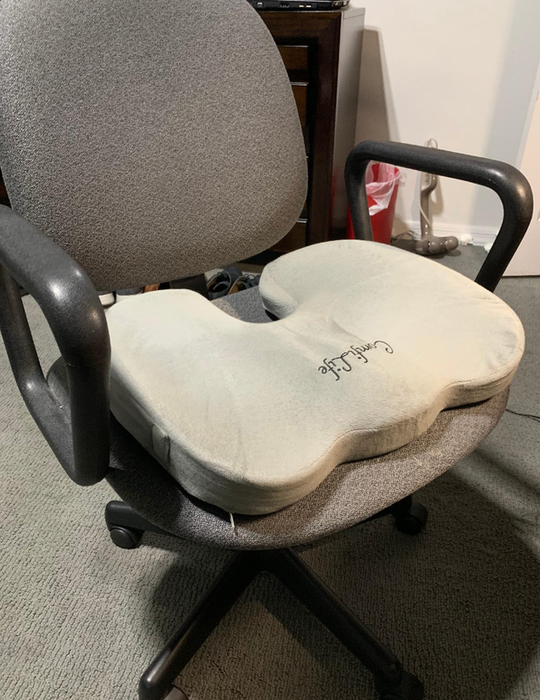 A gray pillow placed on the seat of an office chair