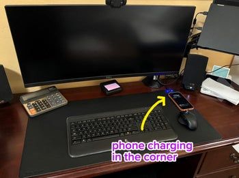 A neatly organized desk featuring a computer monitor, keyboard, mouse, calculator, and a smartphone displaying the time