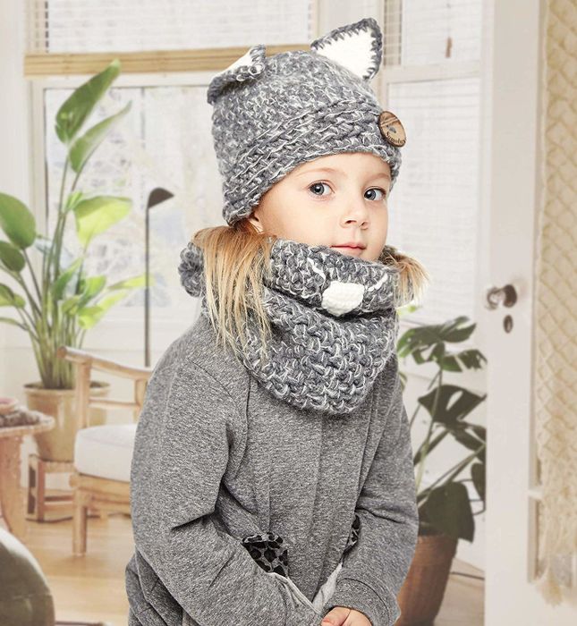 A child model wearing a grey scarf and hat adorned with pointed animal ears.