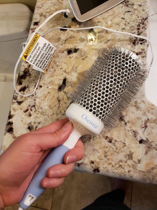 Hand holding an Osensia round hairbrush with a ceramic barrel on a bathroom countertop