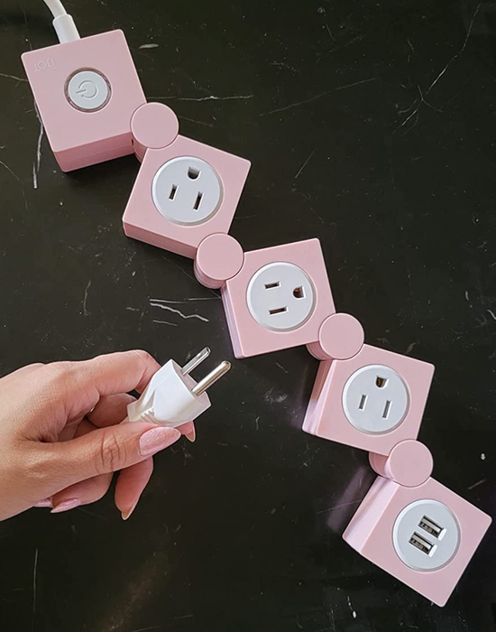 A reviewer holding a pink power strip, with distinct sections for three outlets and two USB charging ports.