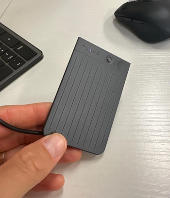 A hand holding a compact, rectangular external solid-state drive (SSD) next to a keyboard and mouse on a desk