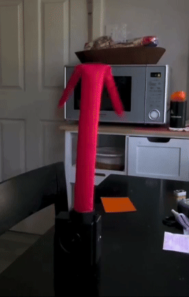 Mini inflatable tube man dancing on a kitchen table, next to a microwave and a pile of papers