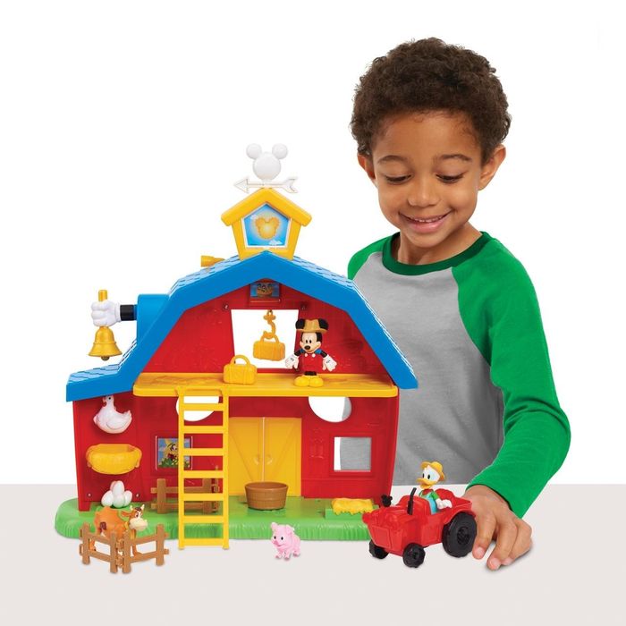 A child pushing Donald Duck in a toy tractor in front of a Disney Junior Mickey Mouse barnyard playset.