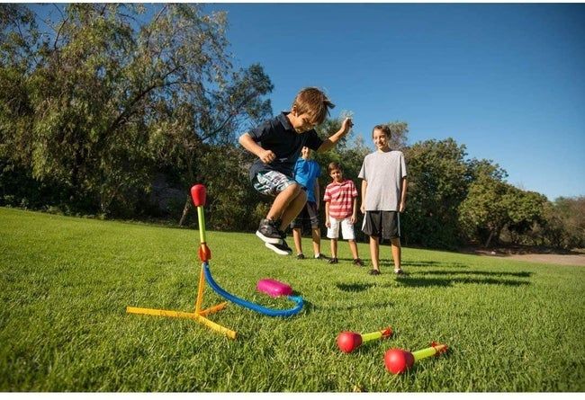 A group of kids eagerly watching as one of them stomps on the rocket’s pad, launching it high into the air.