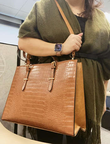 A person carrying a large handbag featuring a brown crocodile-patterned design
