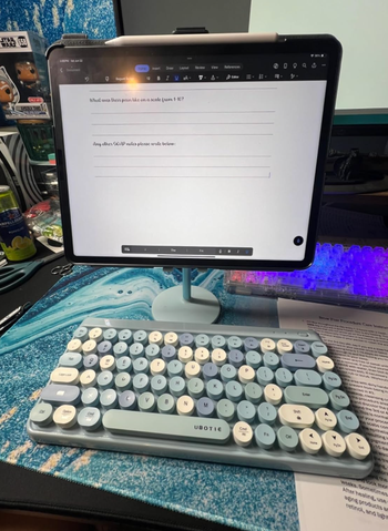 A tablet on a stand displaying a document. A blue and white keyboard labeled
