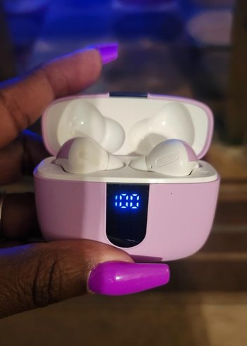 A person holding a pair of wireless earbuds inside an open charging case, showcasing the digital battery level indicator.