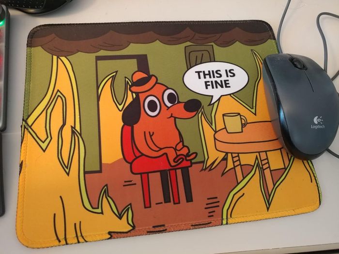 A mousepad featuring the meme of a dog sitting at a table surrounded by flames, with the caption