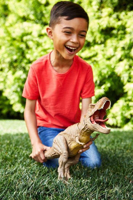 A child playing with a T-rex action figure from Jurassic World in the grass.