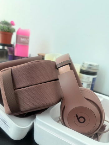 A set of beige over-ear Beats headphones and a matching bag, arranged on a tray surrounded by other items in the background.