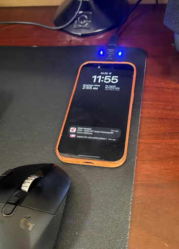 A smartphone on a desk showing a lock screen with notifications, with a computer mouse placed nearby