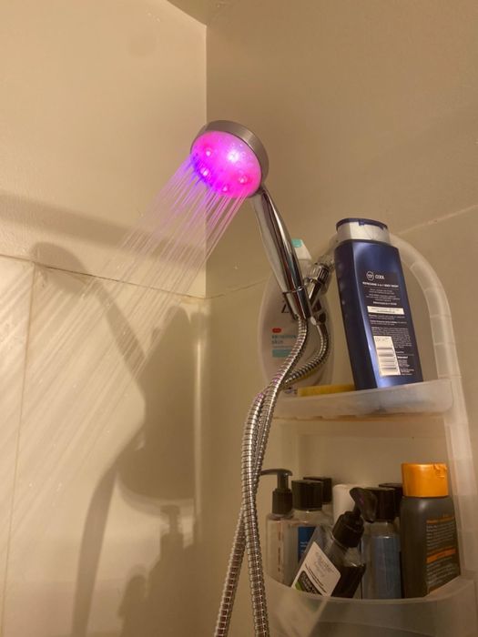 Reviewer’s photo showing the shower head glowing pink in a well-lit room