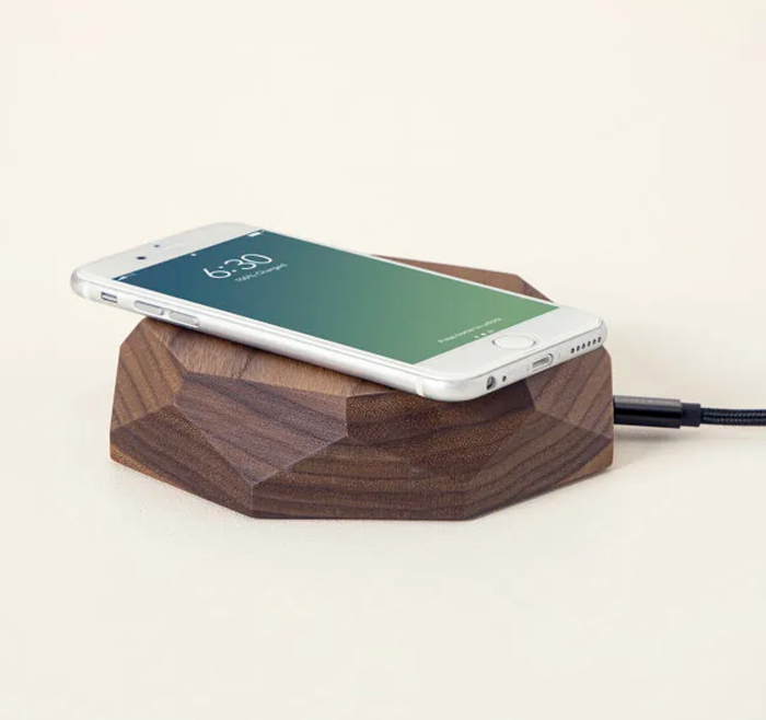 A smartphone placed on a geometric walnut wood charger with a flat surface.
